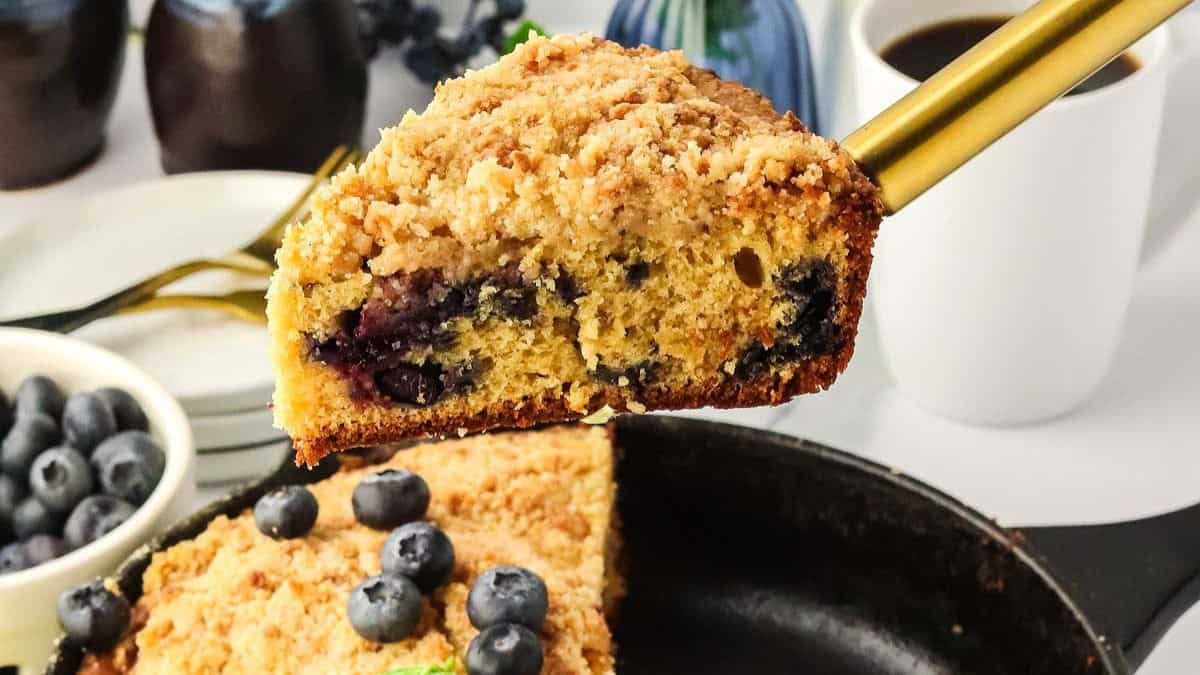 a slice of the thick blueberry crumb cake held over the skillet with the remaining cake