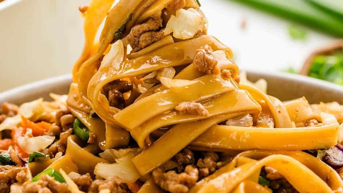 a bowl of thick noodles with ground pork and veggies