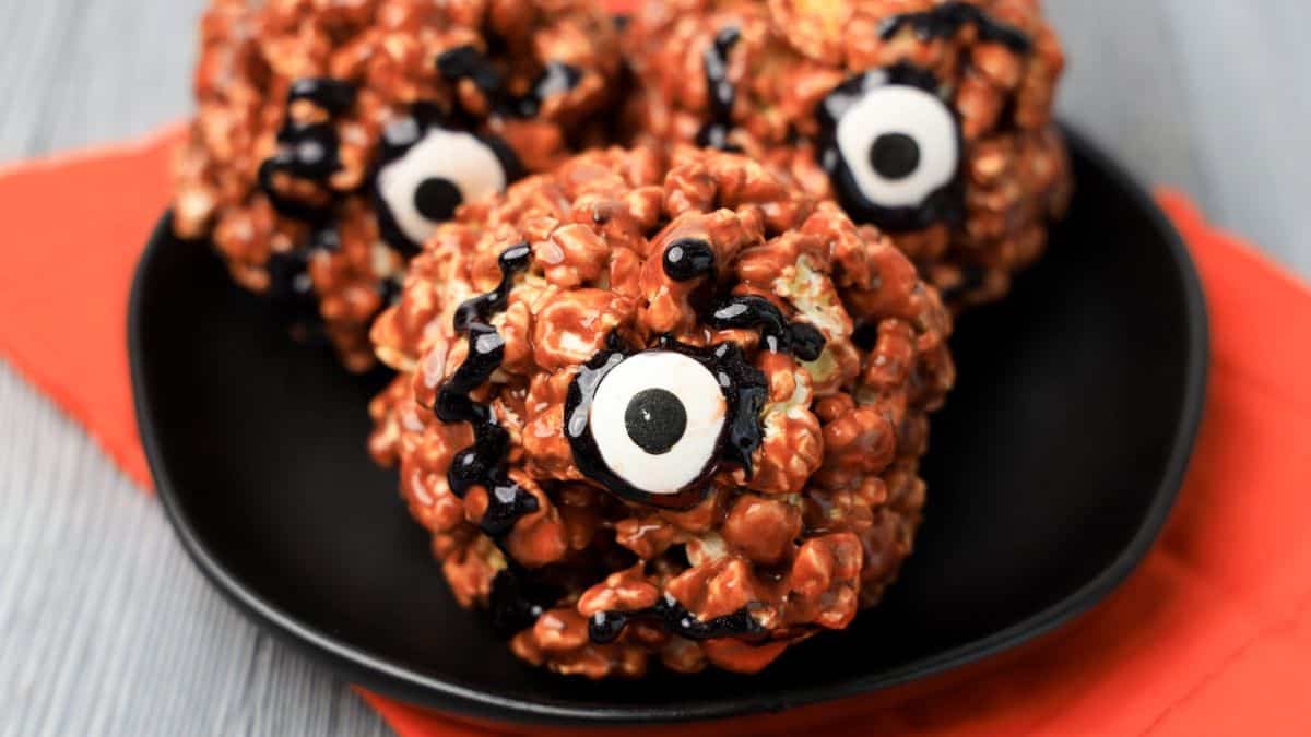 three orange popcorn balls on a plate with a googly eye each