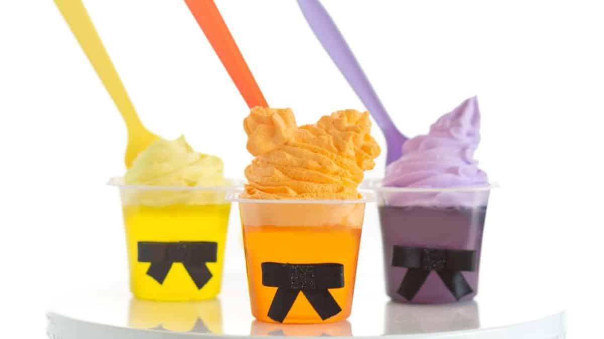 three gelatin cups, one yellow, one orange, one purple topped with frosting