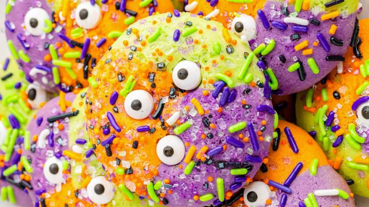 colorful round cookies (yellow green, orange, and purple) with colorful jimmies and googly eyes