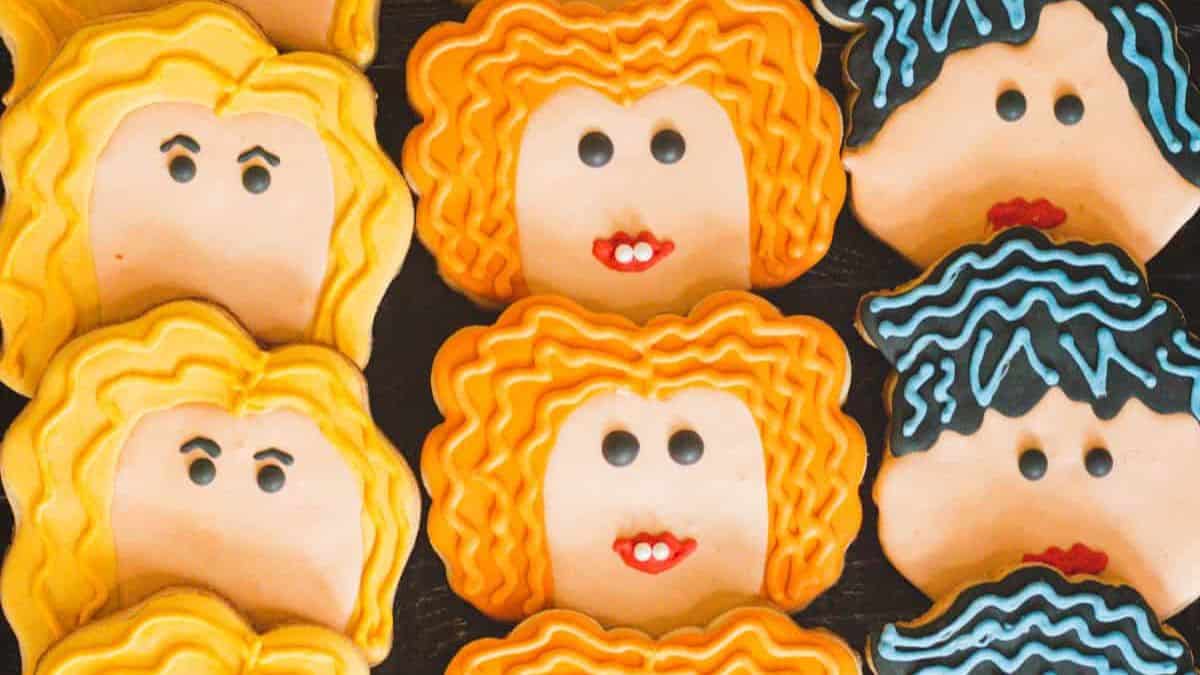 three rows of cookies decorated like portraits of three Sanderson sisters from Hocus Pocus movie
