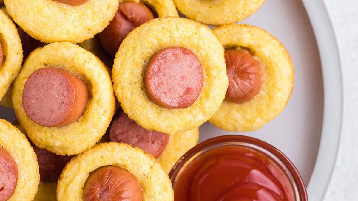 muffins topped with a slice of hot dog and ketchup on the side