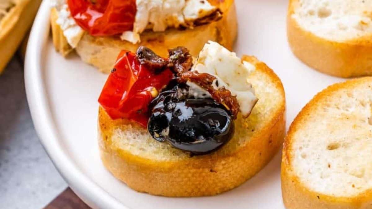 a slice of baguette with baked feta, tomato and olive