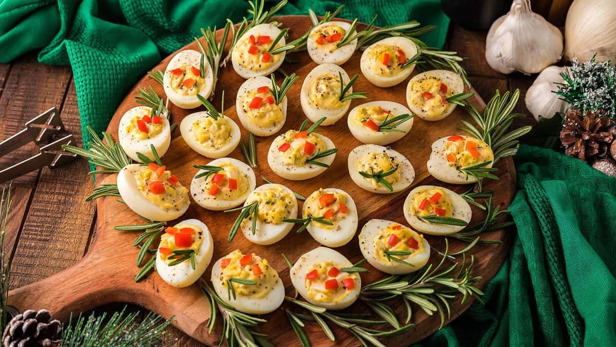 deviled eggs laid out on round wooden board with rosemary sprigs
