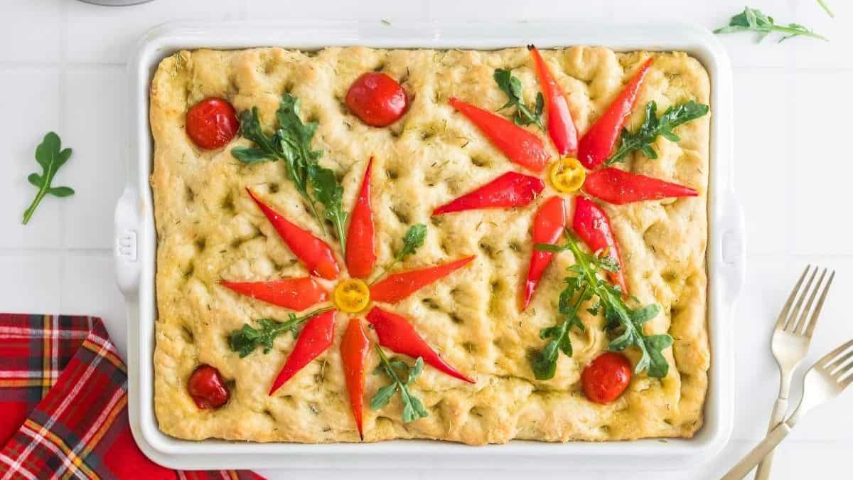 baking dish with focaccia bread with poinsettia decoration made of red bell peppers, arugula and cherry tomatoes