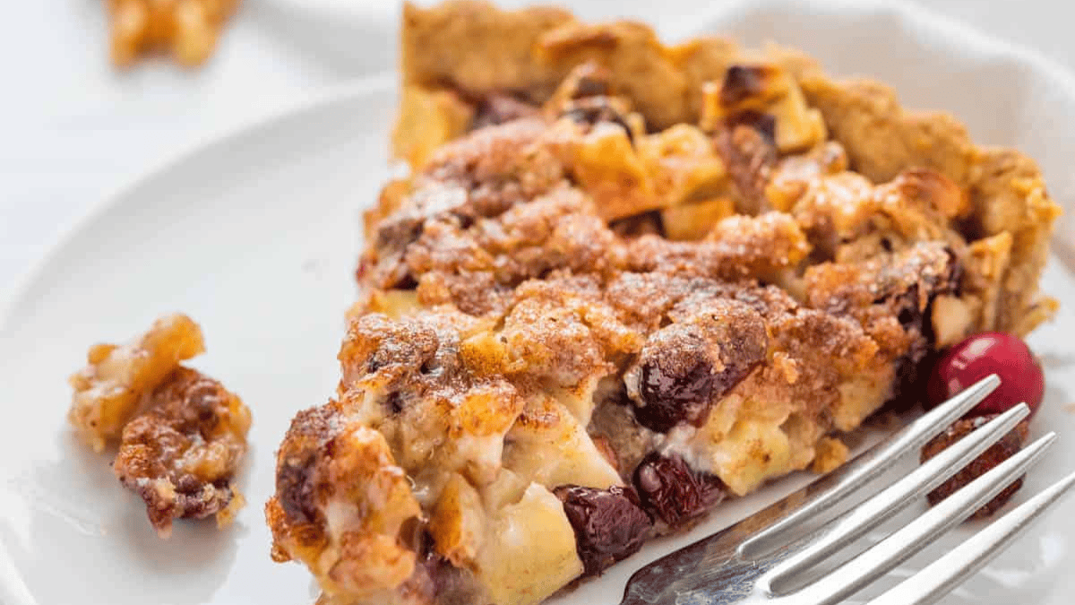 Sliced apple cranberry tart w/ walnut crust plated in white dessert plate.