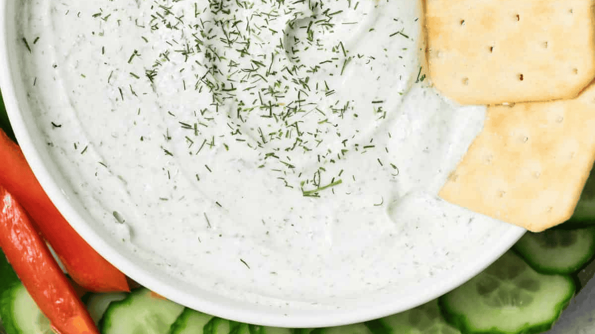 Bowl of Cottage Cheese Ranch Dip with crackers dip on it with cucumber slices