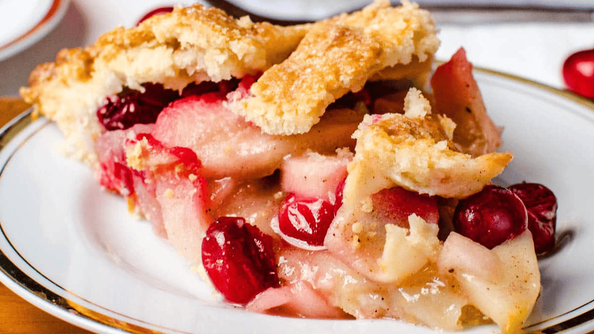 Sliced apple cranberry pie on white with gold lining dessert plate.