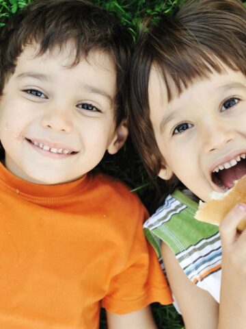 two kids laying on the grass eating sandwiches