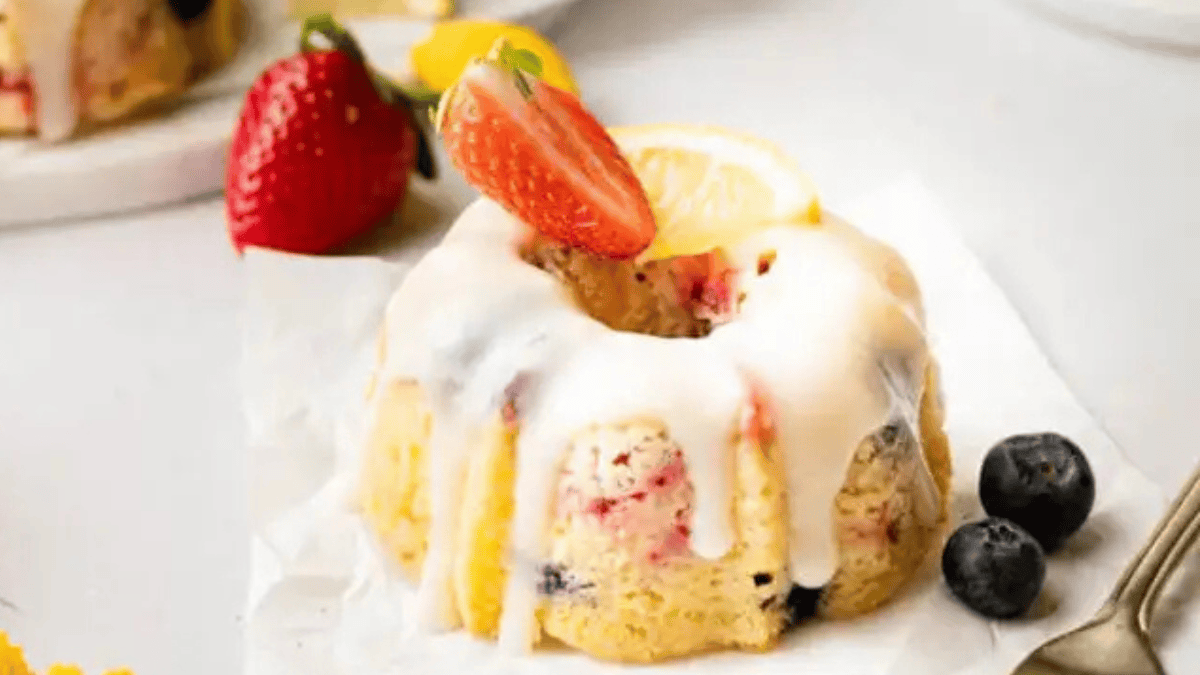 A serving of mini berry bundt cake topped with cream cheese glazed and slice strawberry and lemon.