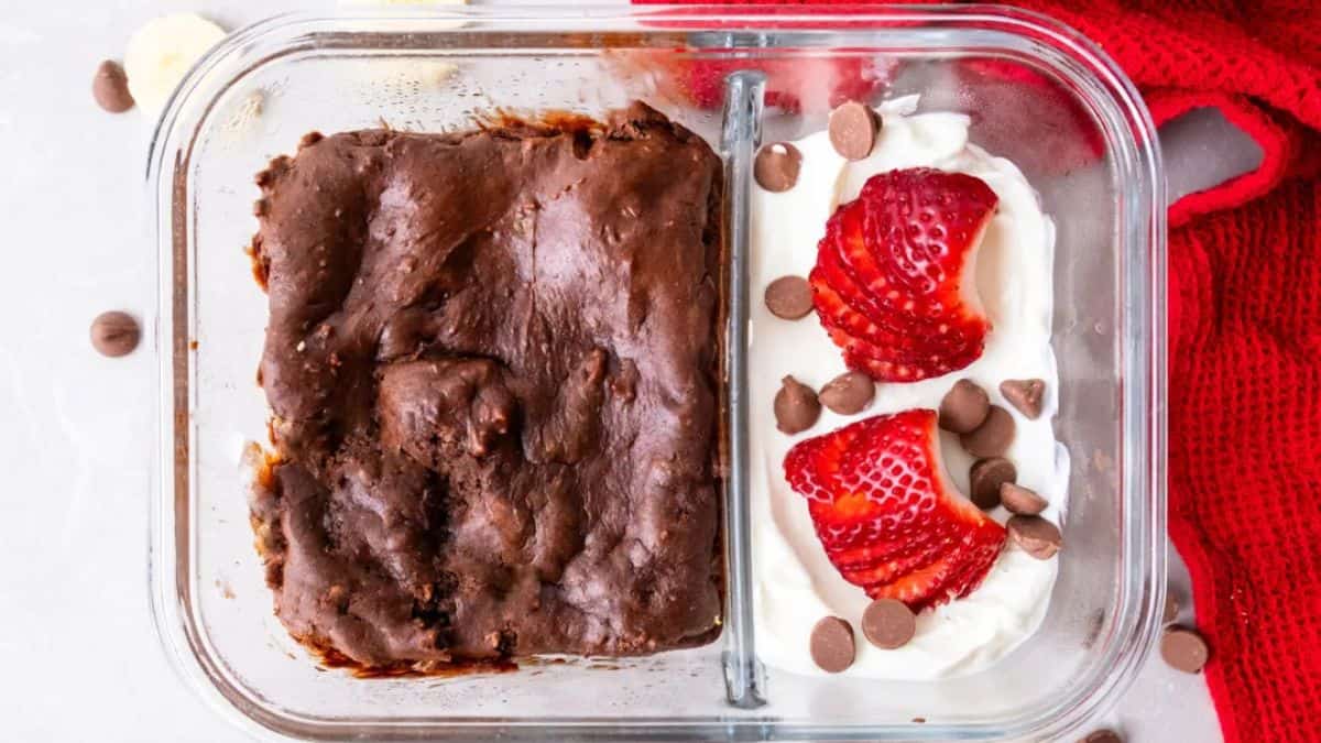Protein brownie in a lunch container with cream with chocolate chips and strawberry on the side.