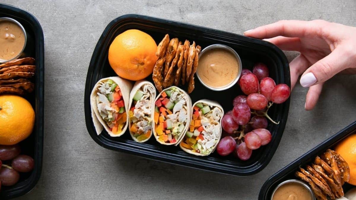 Low carb Thai chicken wraps with fruits and Thai peanut sauce in a black meal container.