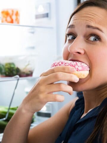 Woman eating a donut looking guilty