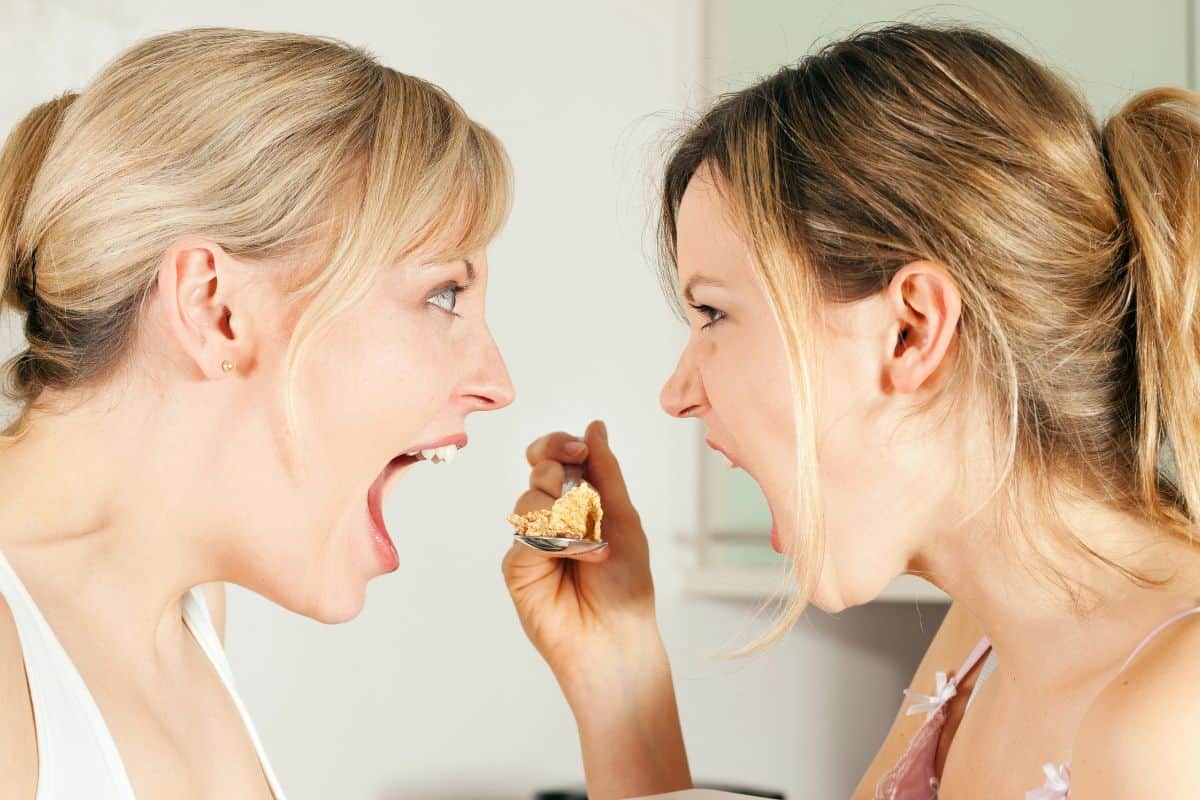two women yelling over a spoon with food on it. 