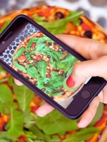 womans hand holding a phone to take a picture of a pizza