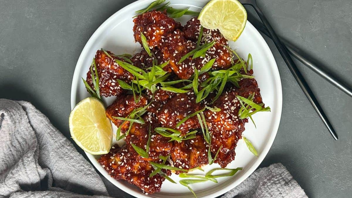 Gorgeously plated crispy gochujang tofu garnish with sesame seeds, fresh onion springs, and lime on the side.