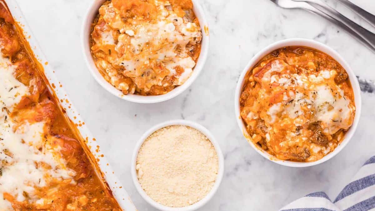 Two bowls of lasagna tater tots and a bowl of parmesan cheese on the side.