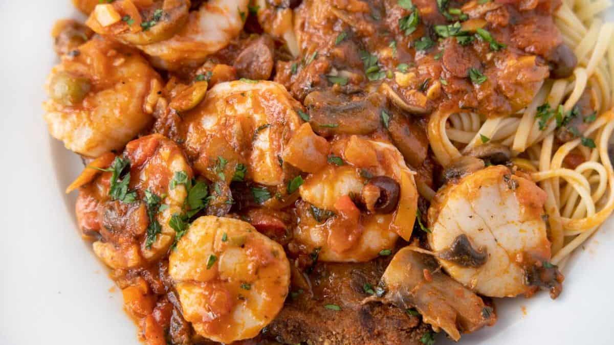 Sicilian style seafood with pasta and eggplant elegantly plated in a classic white plate.