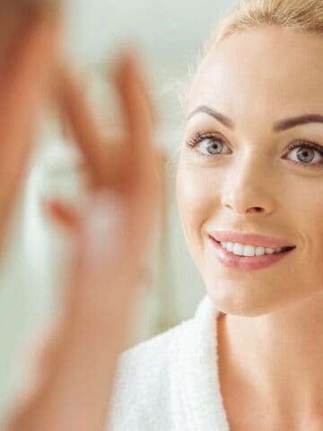 happy woman looking at skin in mirror