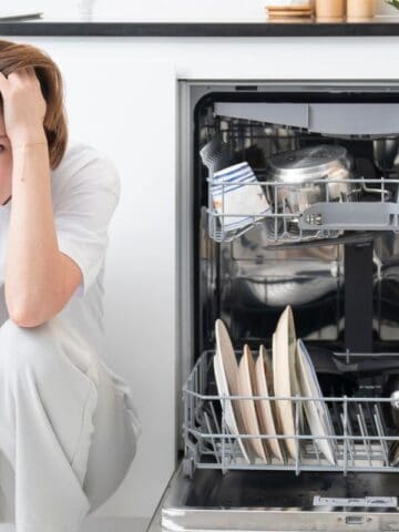 woman holding her head squatting beside the dishwasher