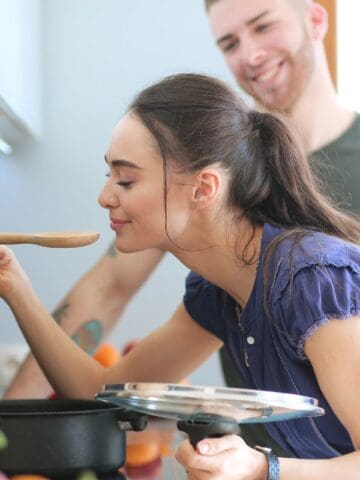 woman smelling soup over a pot, husband behind her smiling