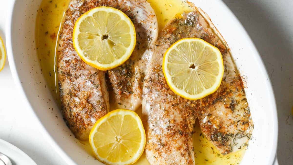 A serving of oven baked tilapia topped with lemons. 