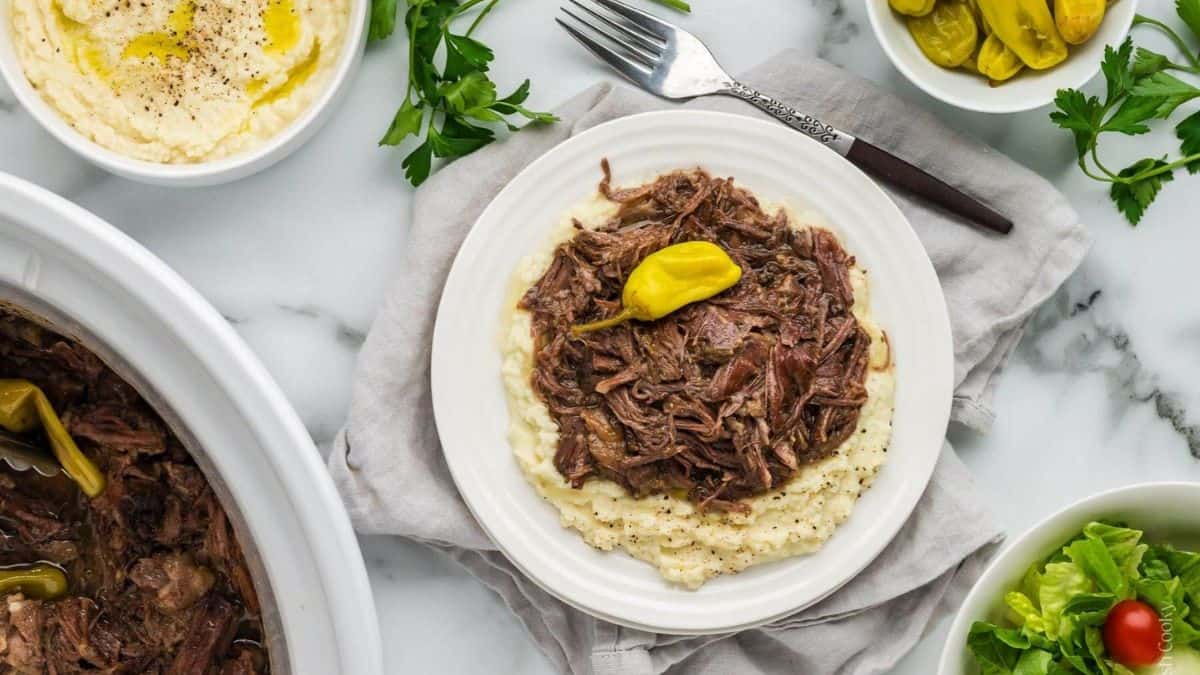A set table with a serving of Crockpot Mississippi Pot Roast in a plate with mashed potatoes.