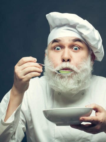 Man Bearded man cook in hat tasting food with spoon in studio on grey background tastes food