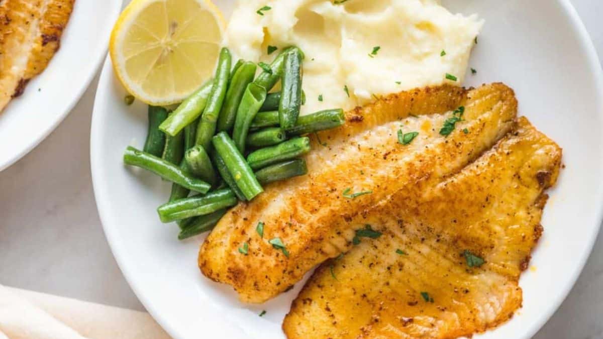A plate of pan fried tilapia with beans and mashed potatoes. 