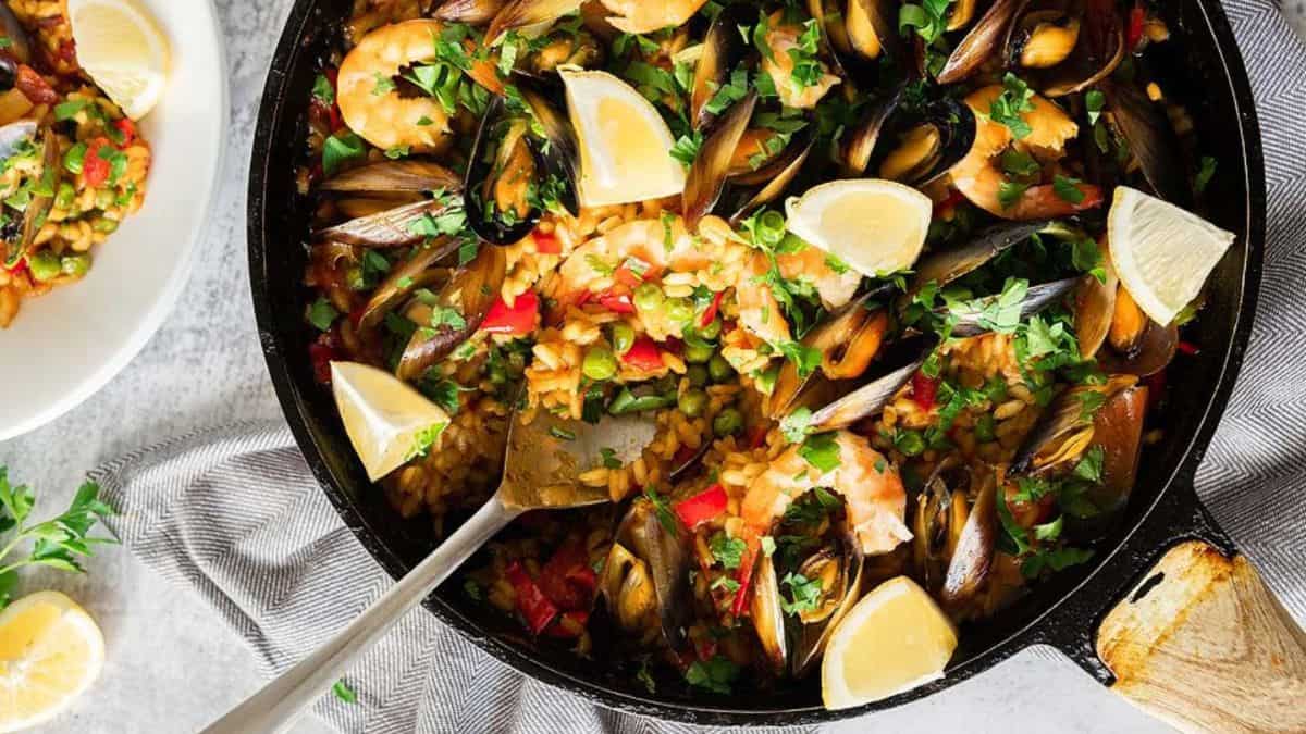 Seafood Paella in a pan with lemons quarters on the side.