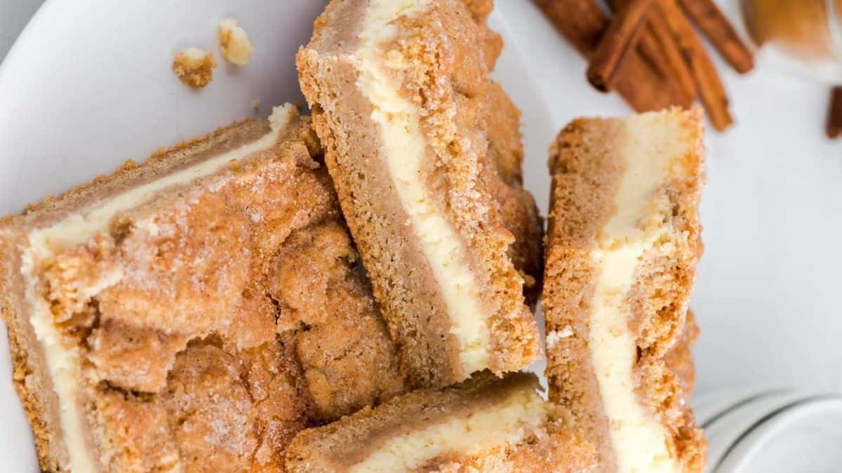 Snickerdoodle cheesecake bars with cinnamon sticks on the side.