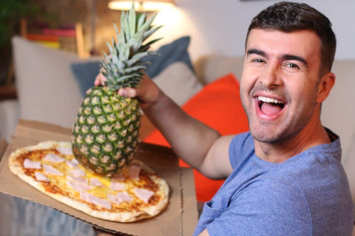 man holding a pineapple on top of a pizza