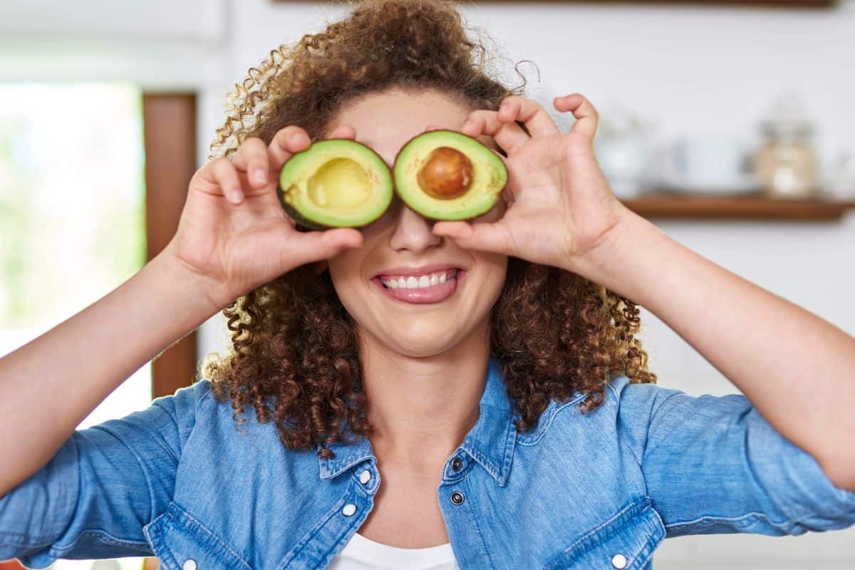woman holding half avocados on her eyes and smiling