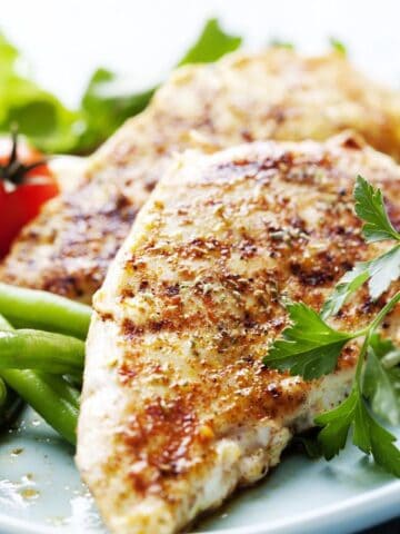 A Plate with chicken breast and veggies around it