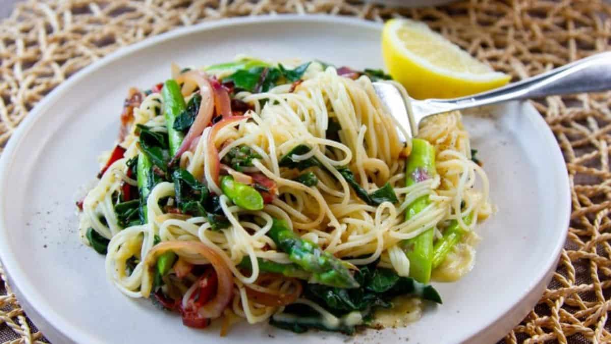 A plate of asparagus pasta with lemon garlic butter sauce with a slice of lemon on the side.