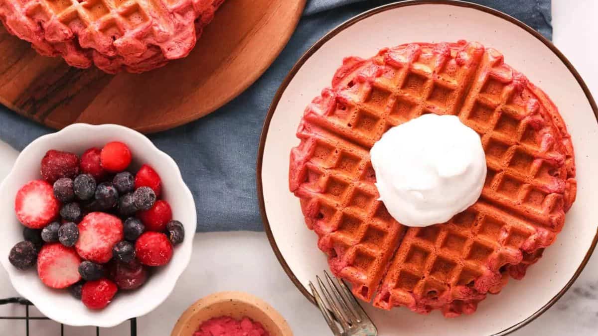 A serving of beetroot waffles topped with some whip cream and berries on the side. 