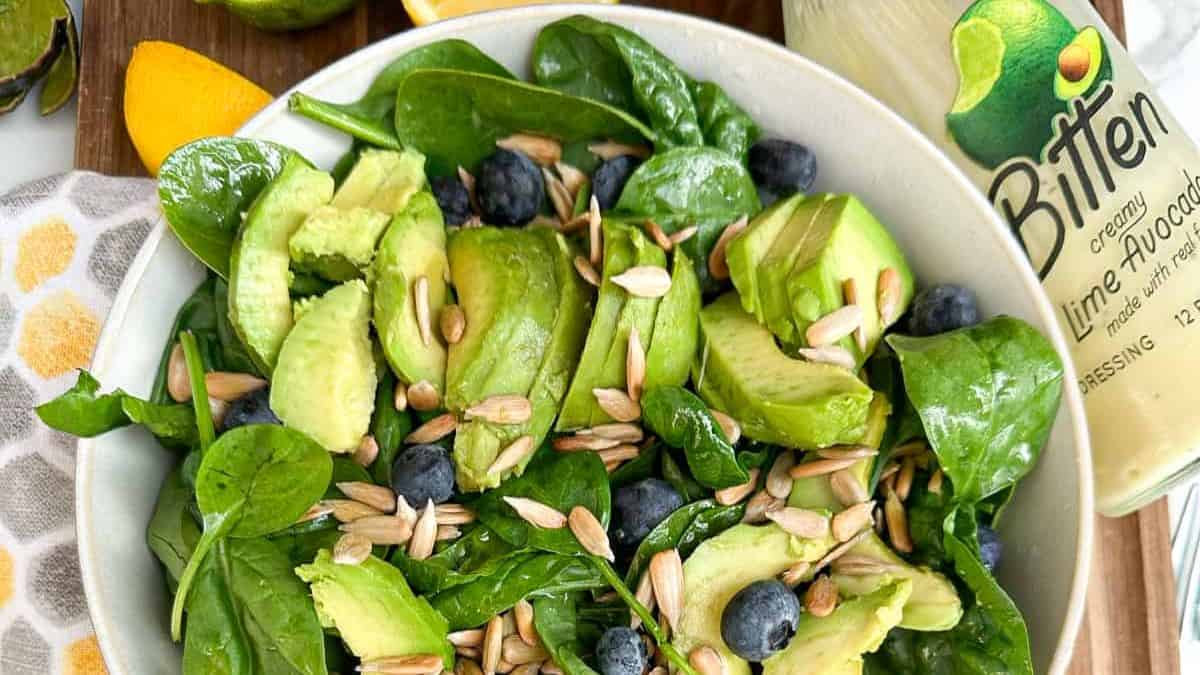 A bowl of spinach avocado salad with toasted sunflower seeds.