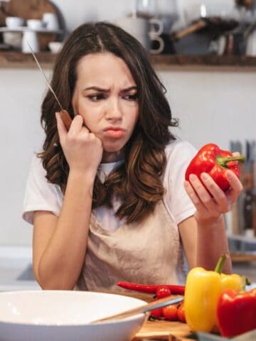 confused woman looking at pepper in kitchen