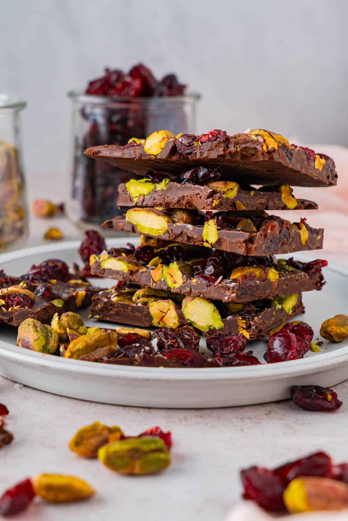 Stack of Chocolate Pistachio Cranberry Bark in a plate with pistachios and dried cranberries