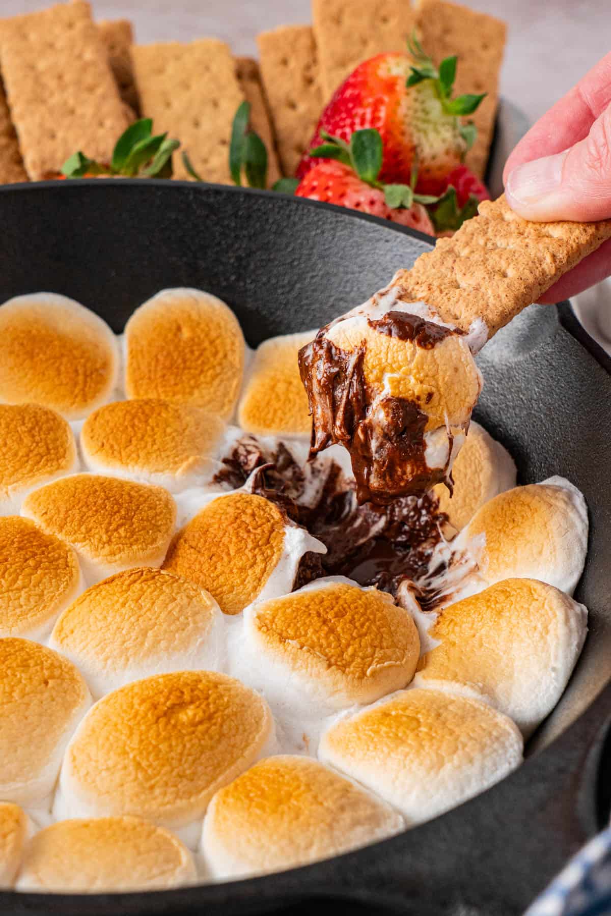 graham crackers dipped on the Easy S'mores Dip in Cast Iron Skillet with crackers and fresh strawberries on the background,