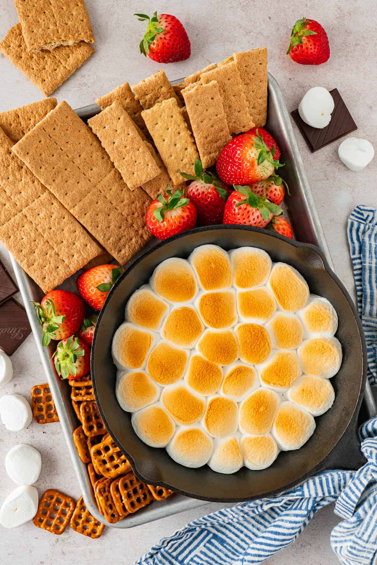 Easy S'mores Dip in Cast Iron Skillet with dippers like graham crackers, strawberries. amd bretzel on the tray/