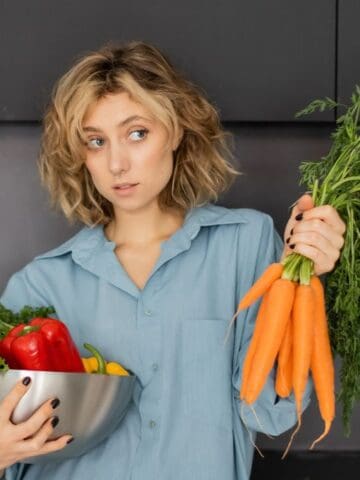 woman looking confused in the kitchen holding vegetables