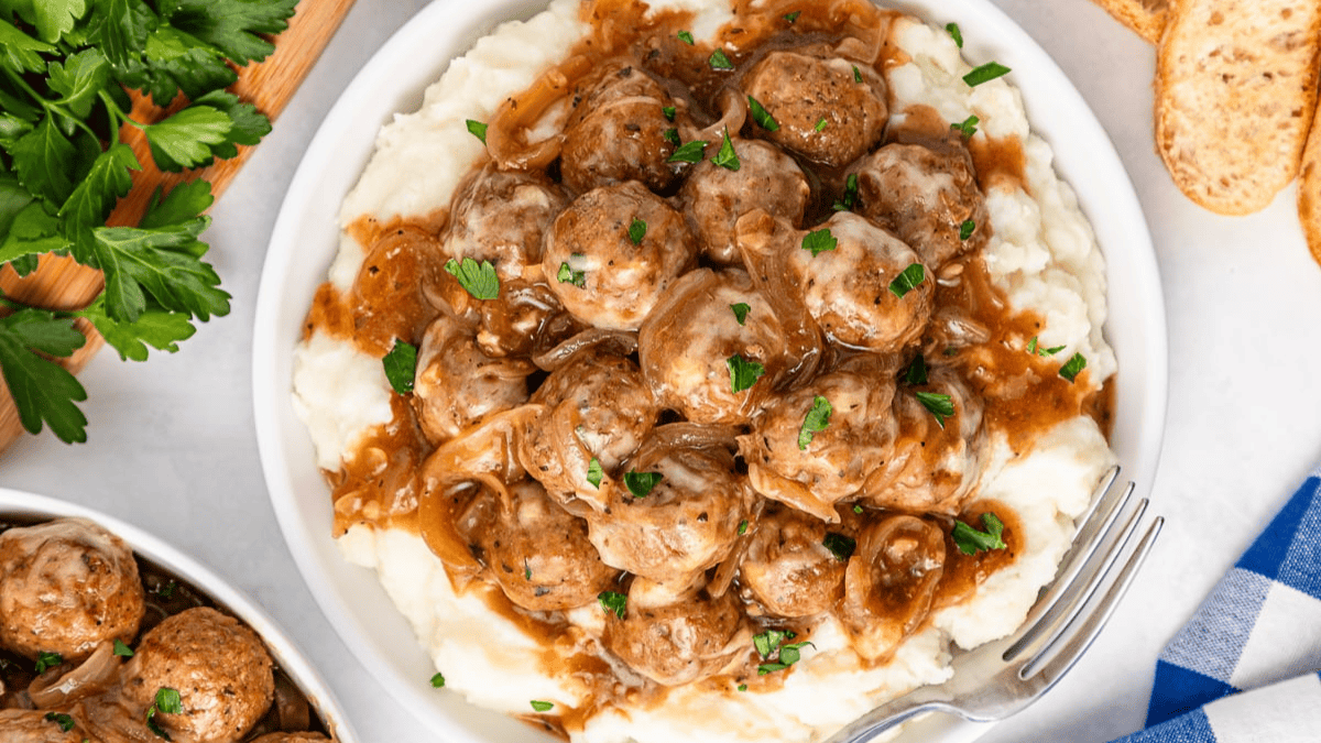 Crockpot French Onion Meatballs, served on top of mashed potatoes on a plate. 