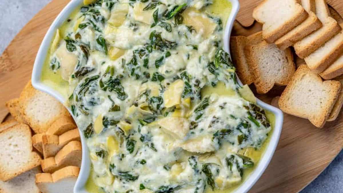 Spinach Artichoke dip served in a bowl with toasted bread on the side.