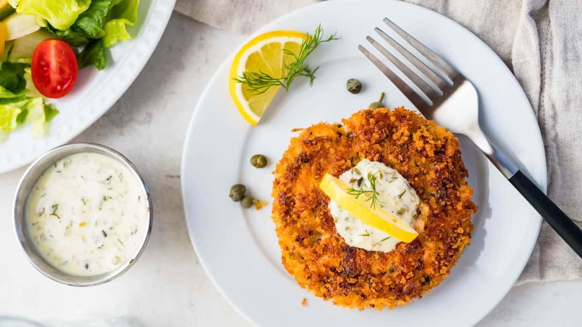 Crunchy Salmon Cake served with a tartar sauce dip and lemon wedges.
