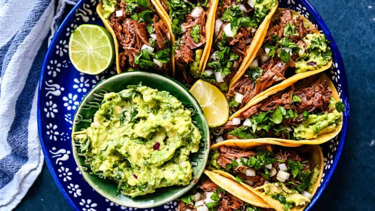 Mexican Shredded Beef Tacos served on a plate with guacamole dip and limes.