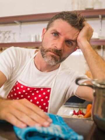 man frustrated in the kitchen wearing a red polkadot apron