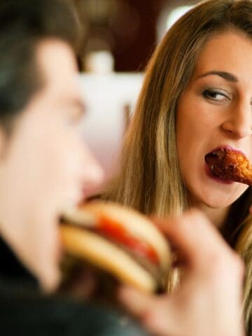 woman and man eating out, woman is mid bite of a wing