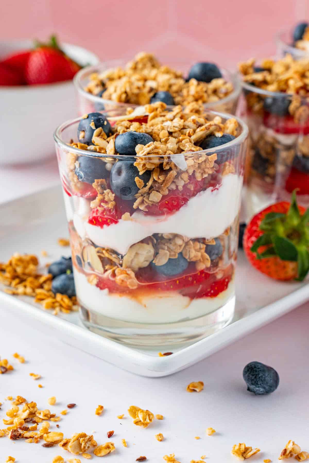 Four servings of Homemade yogurt parfait with berries sitting on a white ceramic platter. 